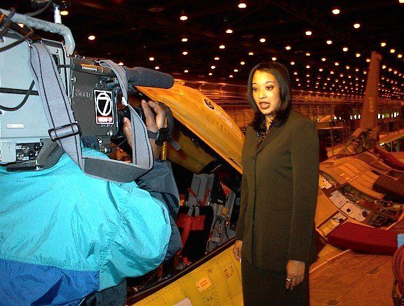 A cameraman is taking a picture of a woman in front of an airplane