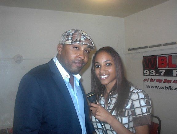 A man and a woman are posing for a picture in front of a sign that says 93.7 fm