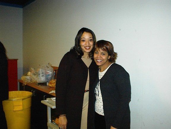 Two women standing next to each other with a yellow trash can in the background