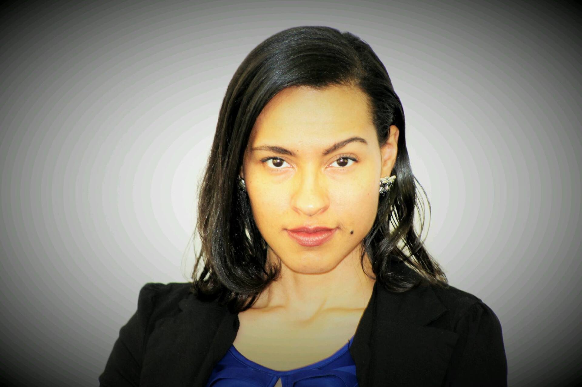 A woman wearing a blue shirt and a black jacket is looking at the camera.