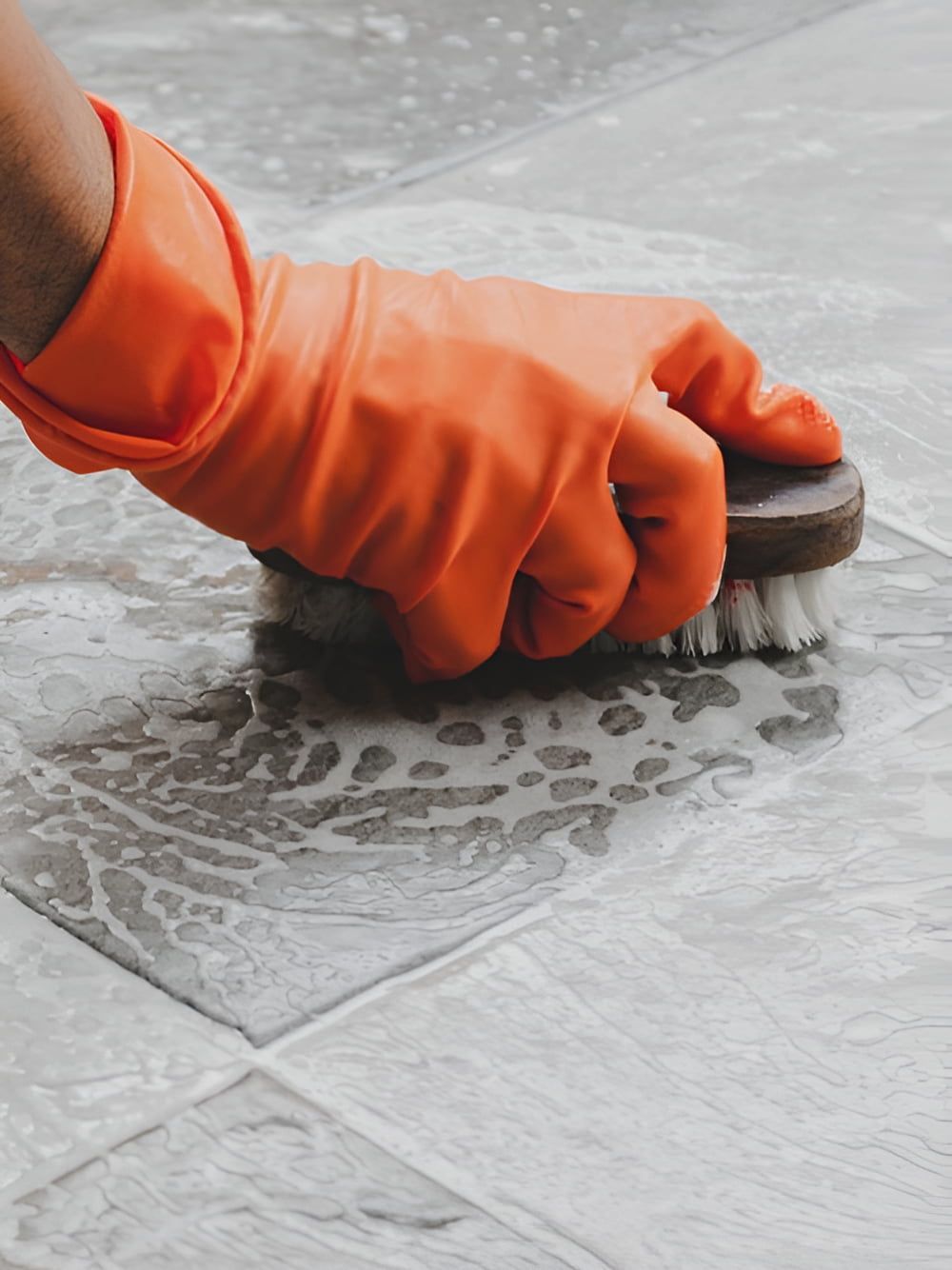 A Person Wearing Orange Gloves Is Cleaning A Tile Floor With A Brush — DP Cleaning Supplies Pty Ltd In Mareeba, QLD