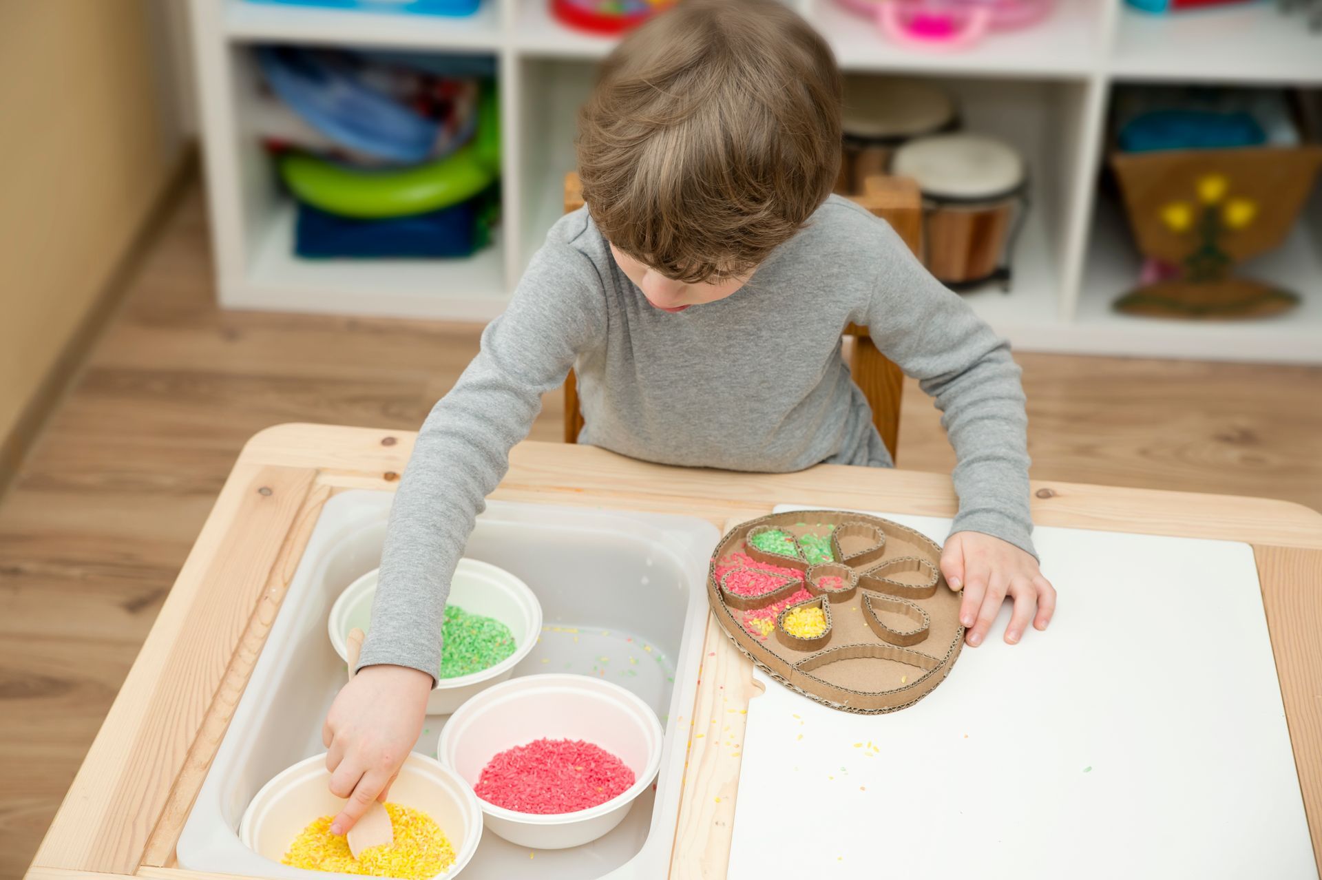 Boy at a table with colored sand, placing it on a cardboard shape.