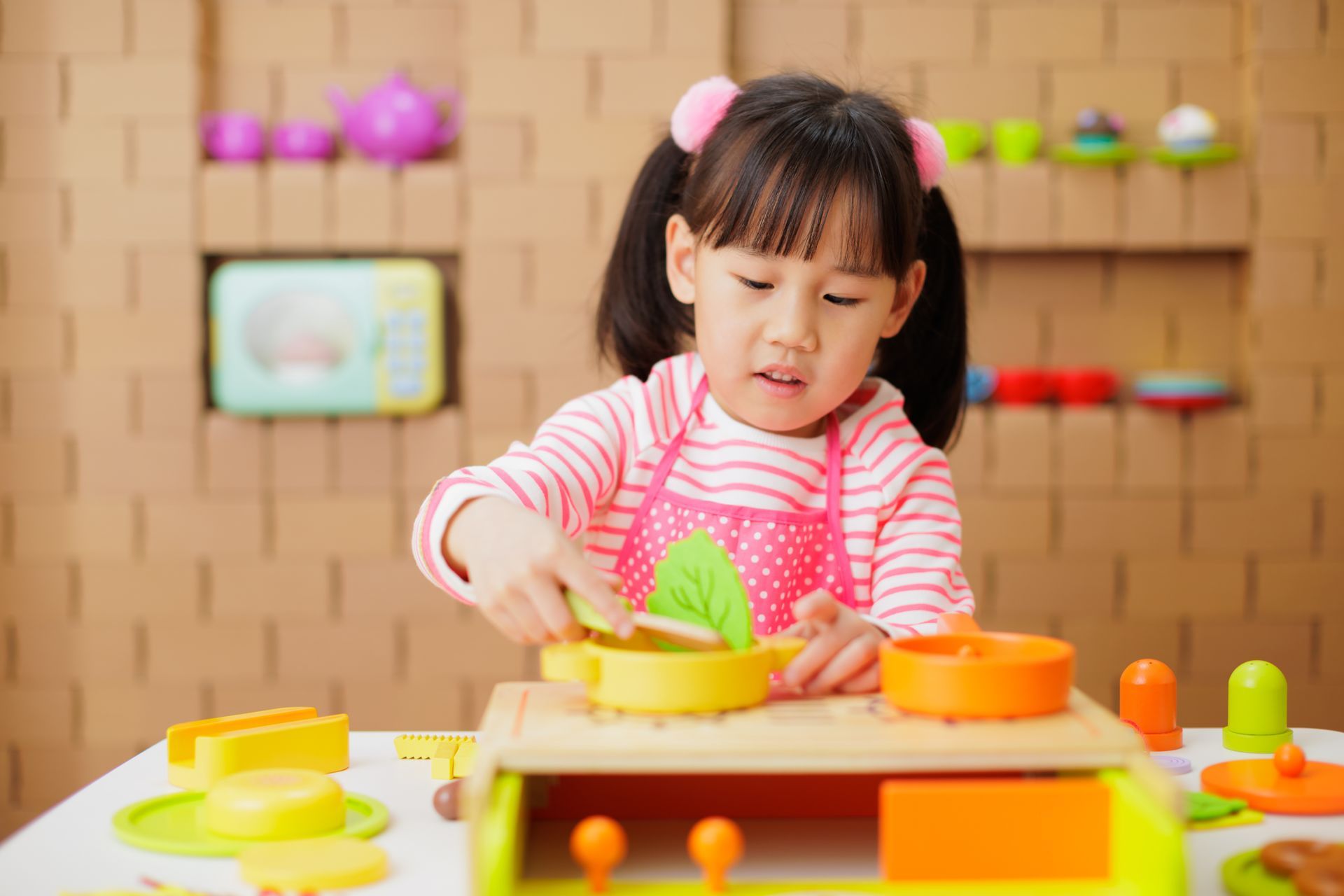 Little girl playing with toy dishes and stacking blocks in a playroom.