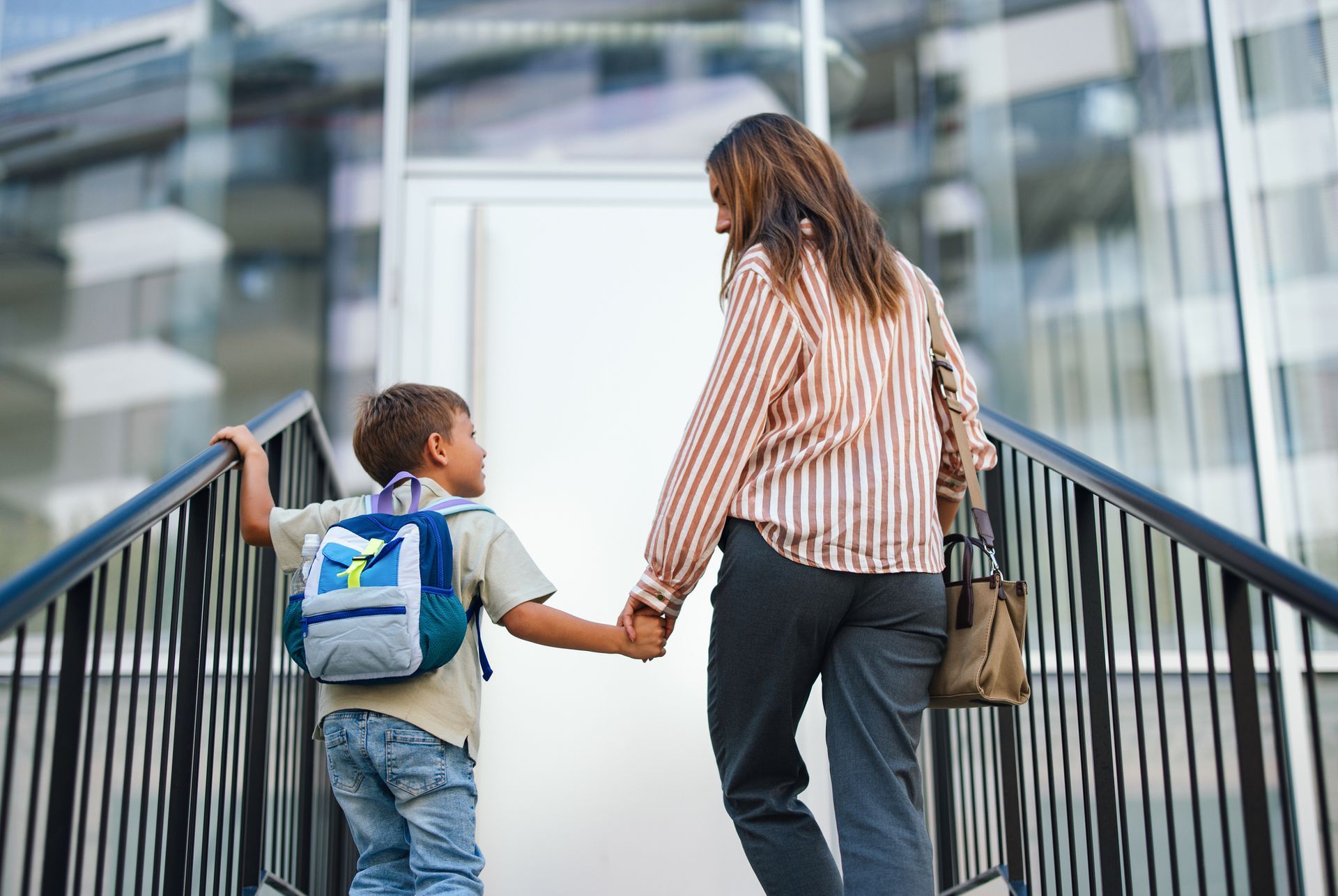 Child with backpack holding adult's hand walking up stairs to building. Child with backpack holding adult's hand walking up stairs to building.