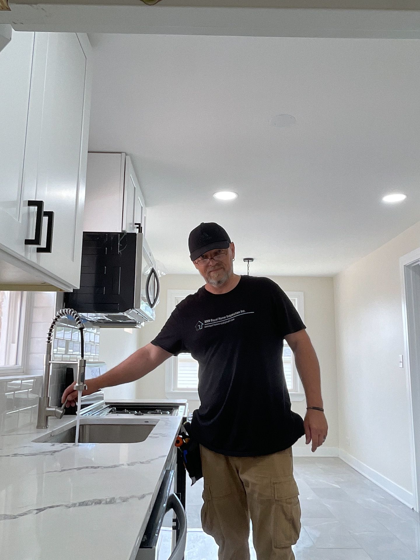 A man in a black shirt is standing in a kitchen next to a sink.