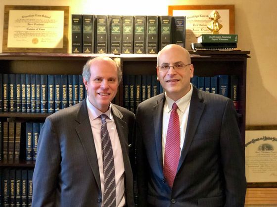 Two men in suits and ties are posing for a picture in front of a bookshelf filled with books.