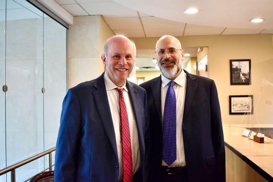 Two men in suits and ties are posing for a picture in front of a bookshelf filled with books.