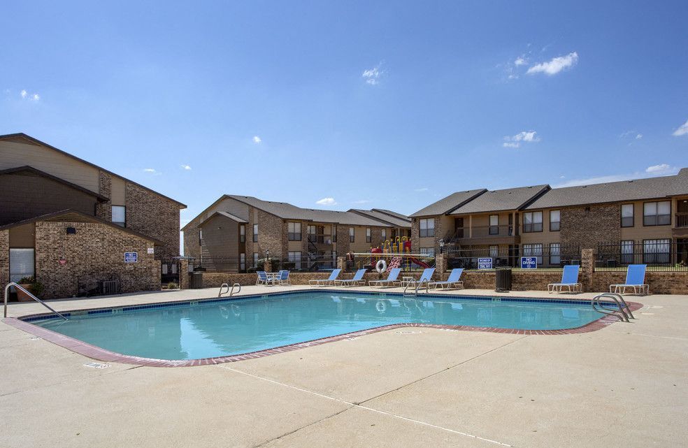 Outdoor apartment pool with lounge chairs and a playground in the background.