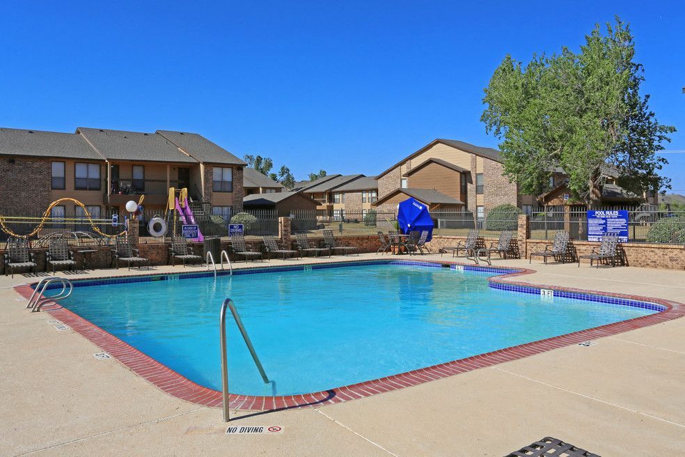 Outdoor community pool at an apartment complex with lounge chairs and a playground.