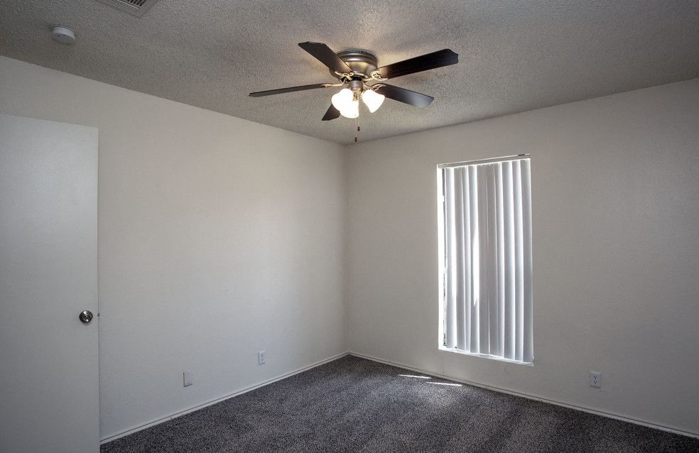 Empty bedroom with white walls, carpet, a ceiling fan, and vertical blinds over the window.