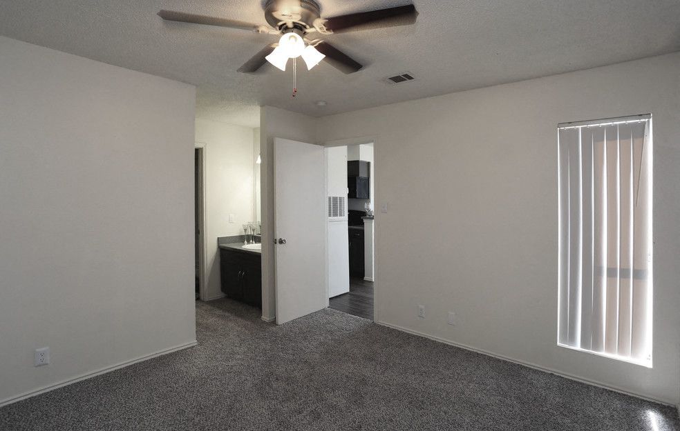 Carpeted living room in an apartment with a ceiling fan and doorway to the kitchen.