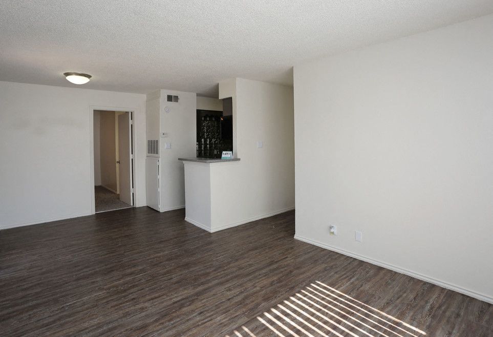 Empty living area with laminate flooring, a small kitchen counter, and an adjacent doorway.