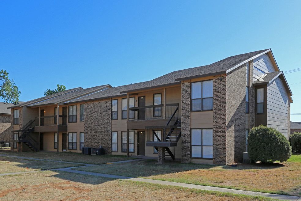 Exterior view of a two-story apartment building with brick accents, balconies, and external staircases.