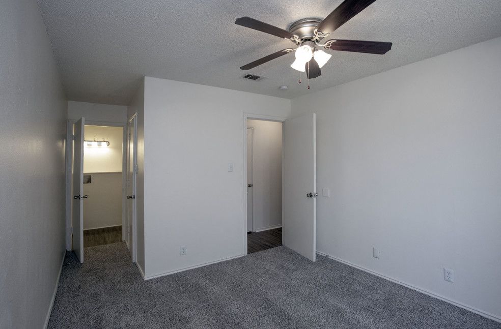 Empty bedroom with gray carpet, white walls, and a ceiling fan; two doors open to the hallway.