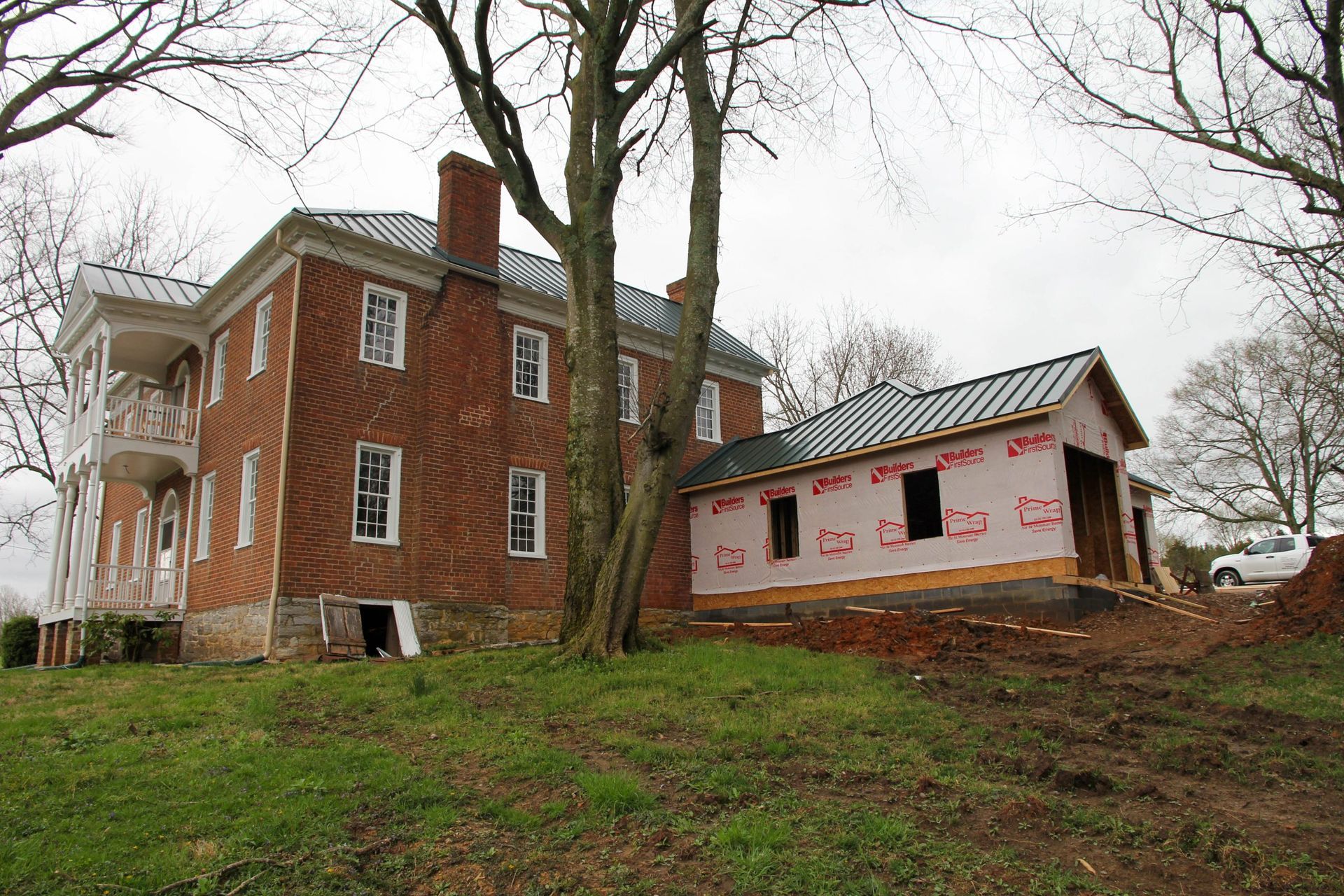 A historic brick house under renovation with a new, unfinished wing covered in pink protective sheathing.