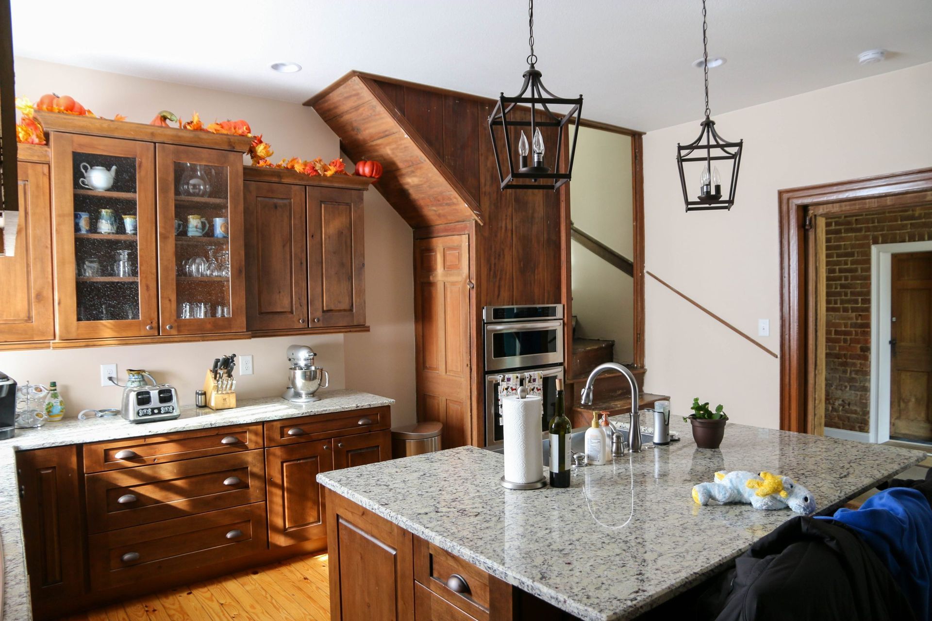 A kitchen with brown wooden cabinets, granite countertops, an island with a sink, and two pendant lights.