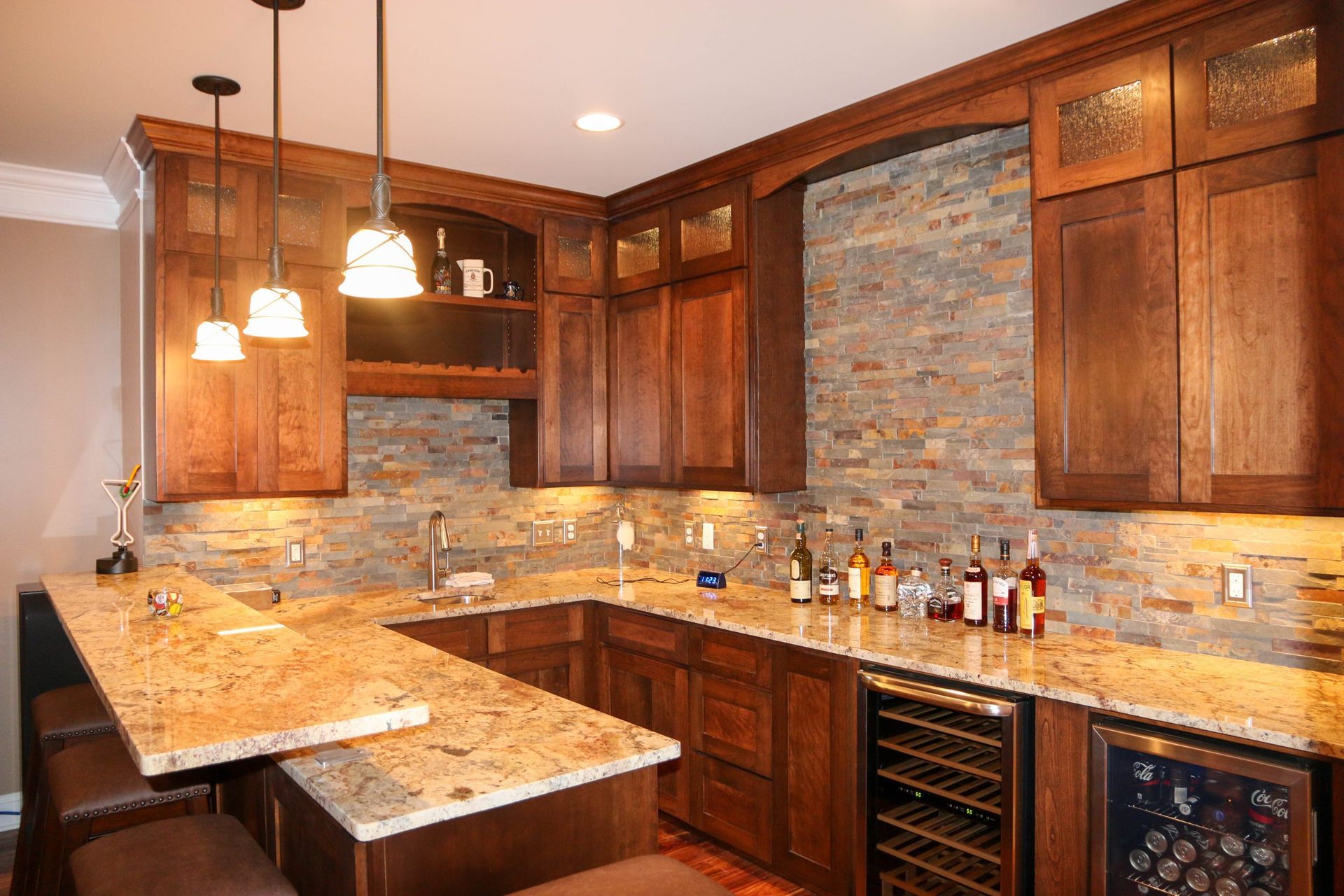 A wet bar featuring wooden cabinets, granite countertops, stone backsplash, and three hanging pendant lights.