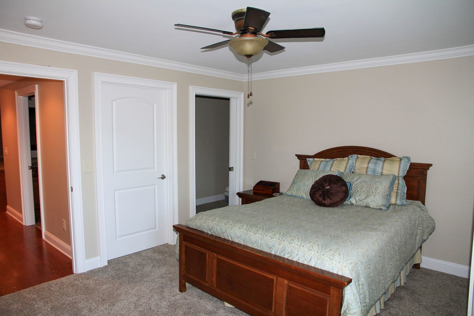 A bedroom with a wooden bed, patterned bedding, a ceiling fan, and open doorways to a hallway and closet.