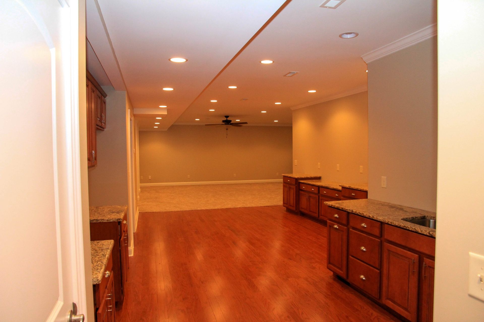 A wide-angle view of a finished basement featuring hardwood floors in the foreground and carpeted area in the back.