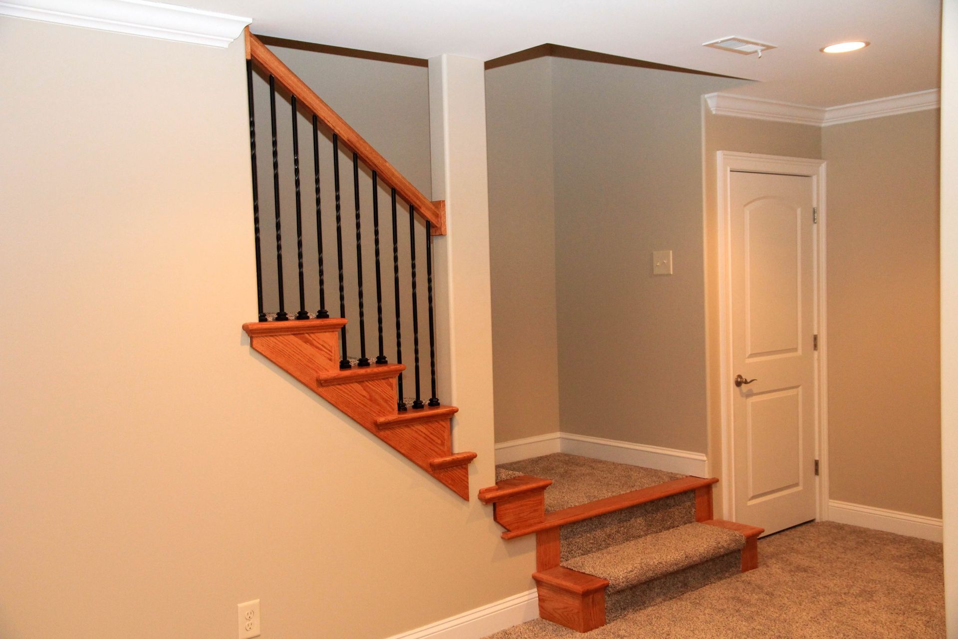 A set of indoor stairs with wooden steps, black railings, and tan carpet, leading to a closed white door.