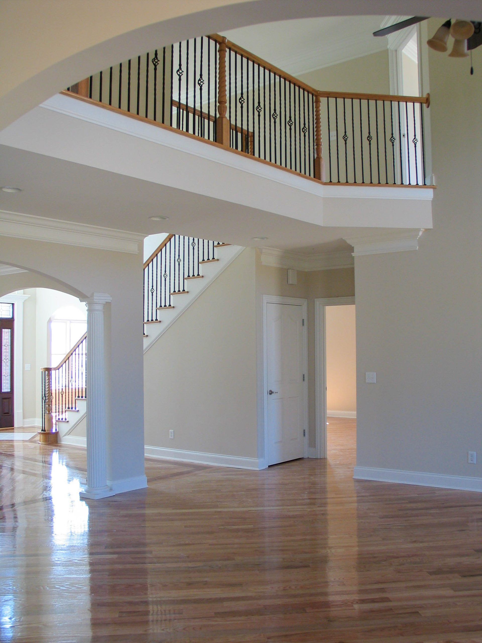 An interior view of a home with light walls, hardwood floors, a wooden staircase, and an upper-level balcony railing.