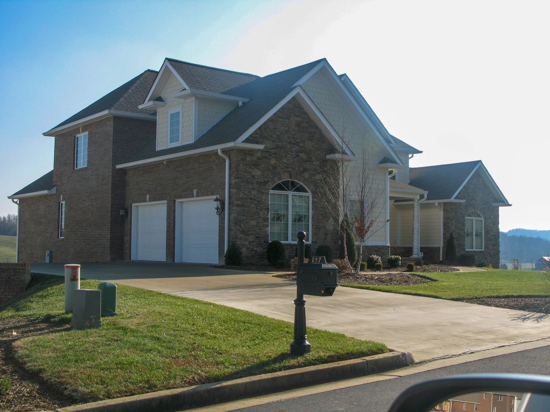 A two-story suburban house with a brick and beige facade, featuring a two-car garage and a concrete driveway.