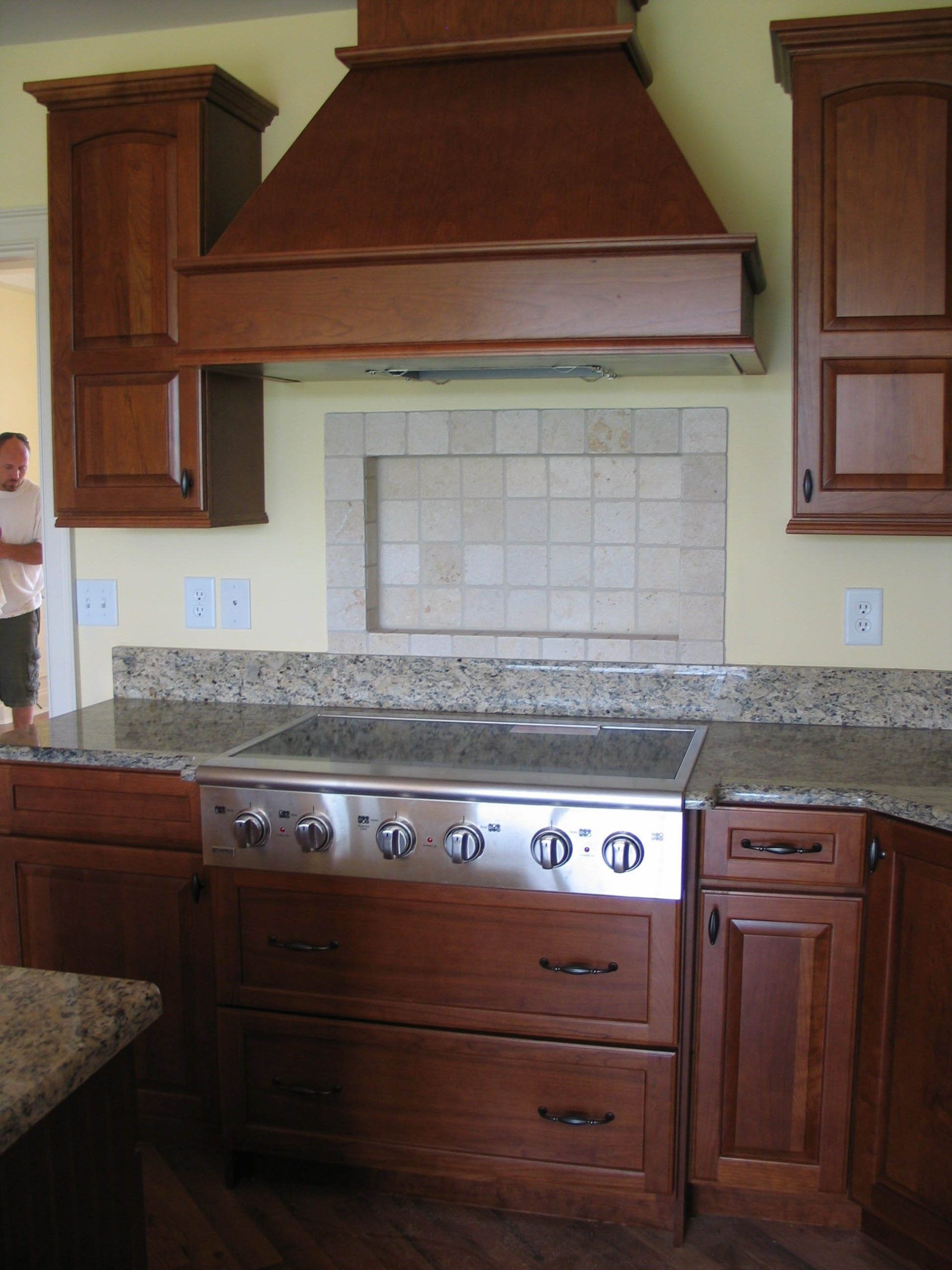 A kitchen featuring a stainless steel stove, dark wood cabinets, a granite countertop, and a tiled backsplash.