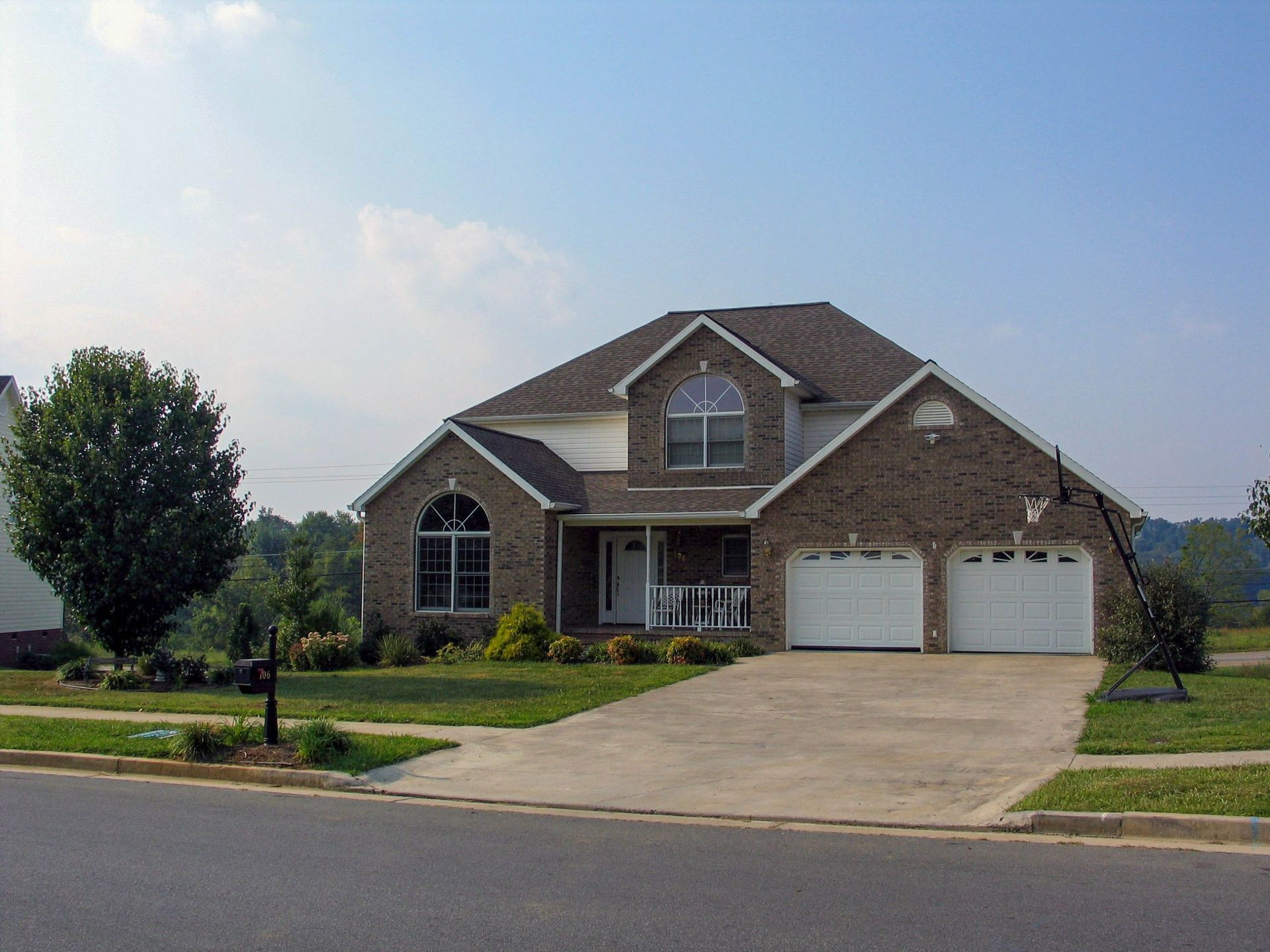 A brown brick house with a white garage and a green lawn under a clear blue sky.