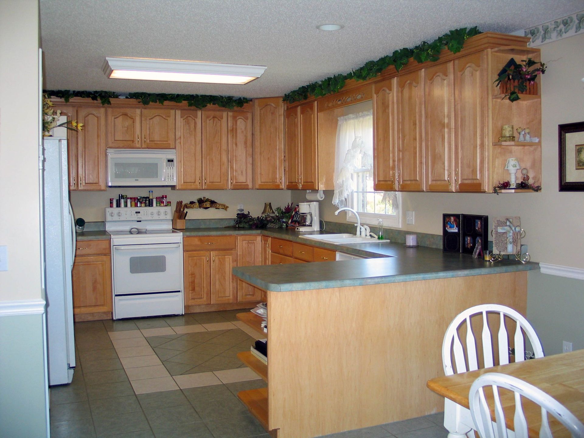 A kitchen with light wood cabinets, white appliances, green countertops, and a dining table with chairs in the foreground.
