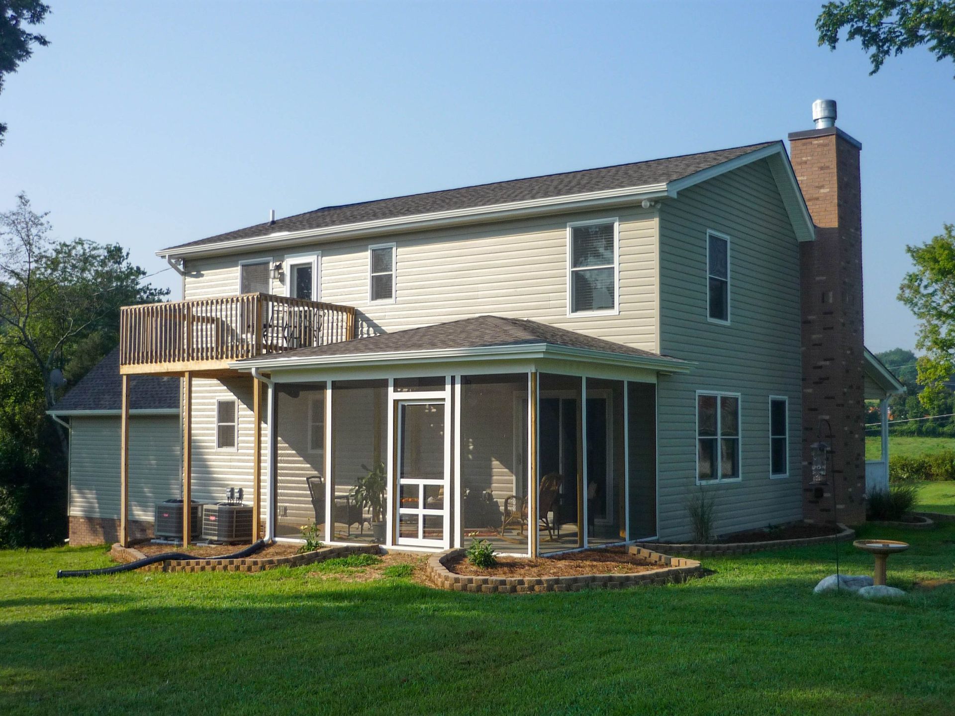 Two-story house with light-colored siding, a brick chimney, a small upper deck, and a ground-floor screened-in porch.