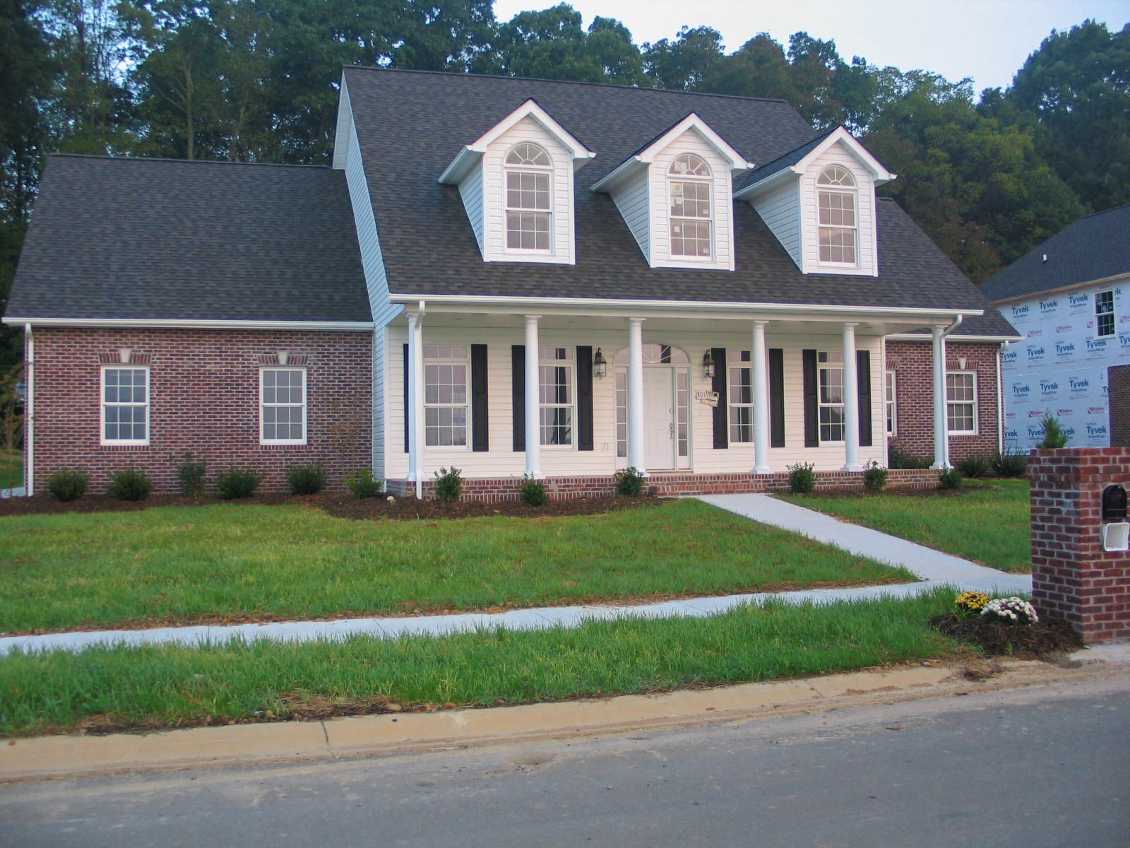 A two-story house with a brick facade on the left and a white porch and siding on the right, under a gray shingled roof.