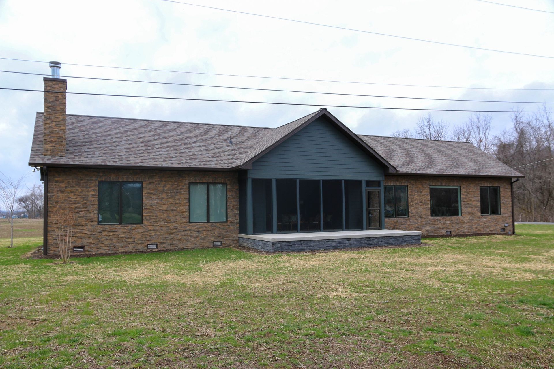 A brick ranch-style house with a gray shingled roof, a chimney on the left, and a central screened-in porch.