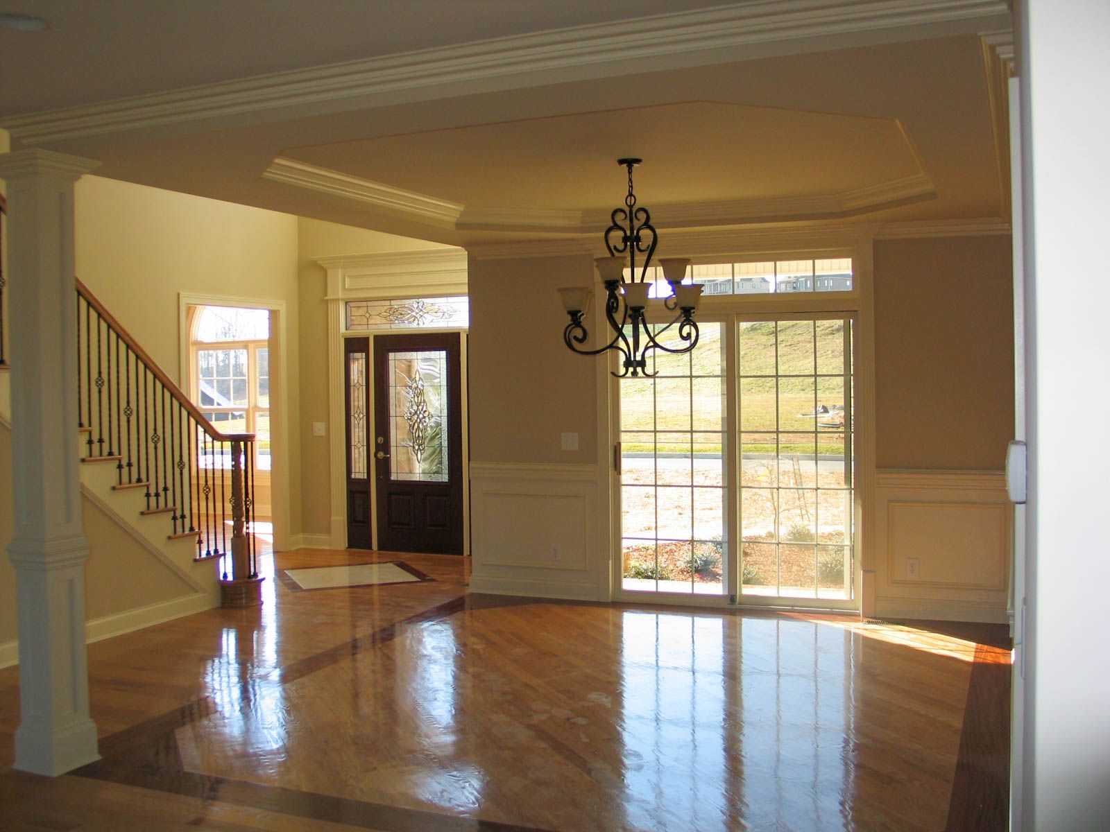 A bright, open dining area with hardwood floors, a hanging chandelier, wainscoting, and a view of a staircase and entryway.