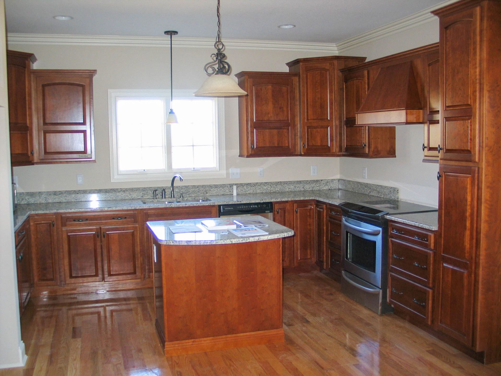 A kitchen with wood cabinets, granite countertops, a central island, and hardwood floors.