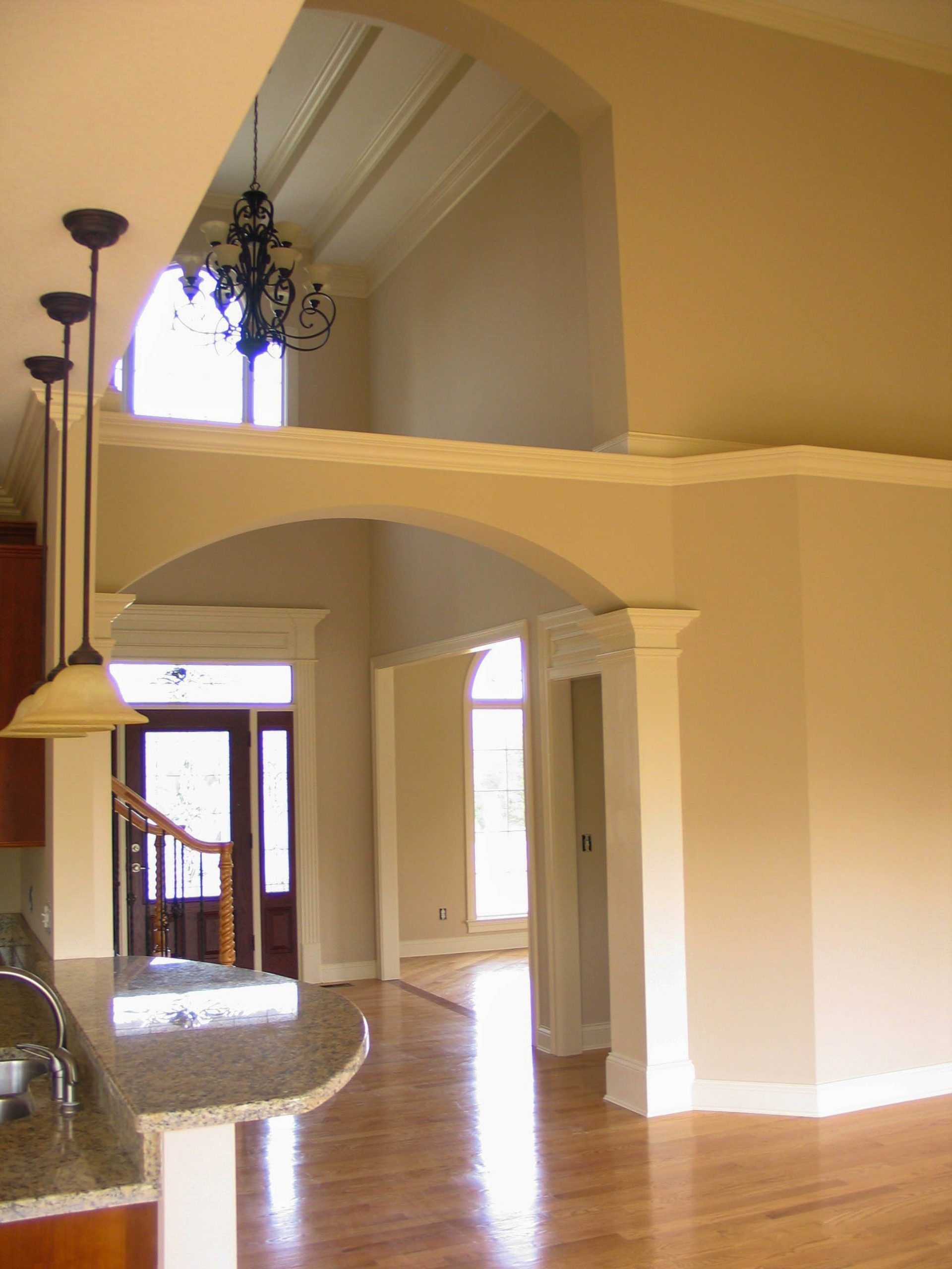 Interior view of a living space with a large archway, beige walls, wooden floors, and a hanging chandelier.