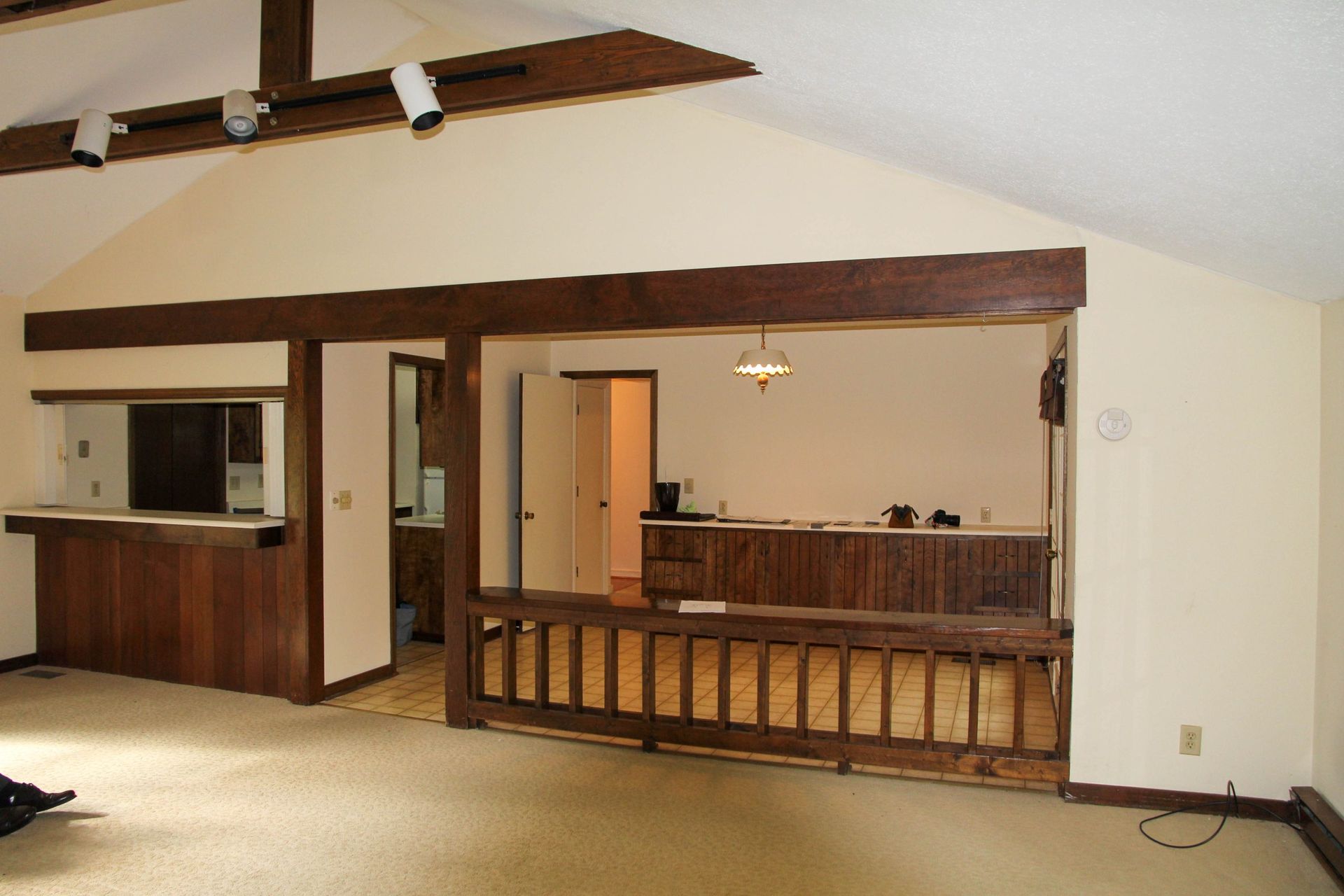 An interior view of a living area featuring a raised, open room with dark wood accents and railings, carpeted flooring.