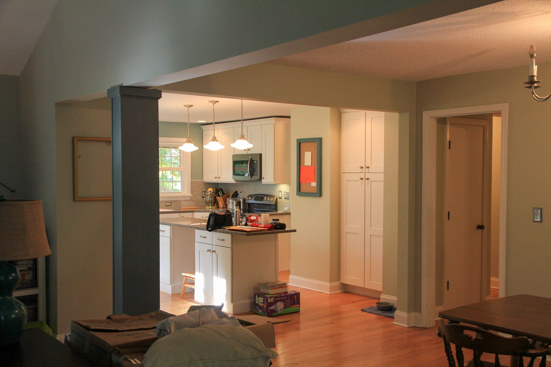 An open-concept view from a living area toward a bright kitchen with white cabinetry, a center island, and wood flooring.