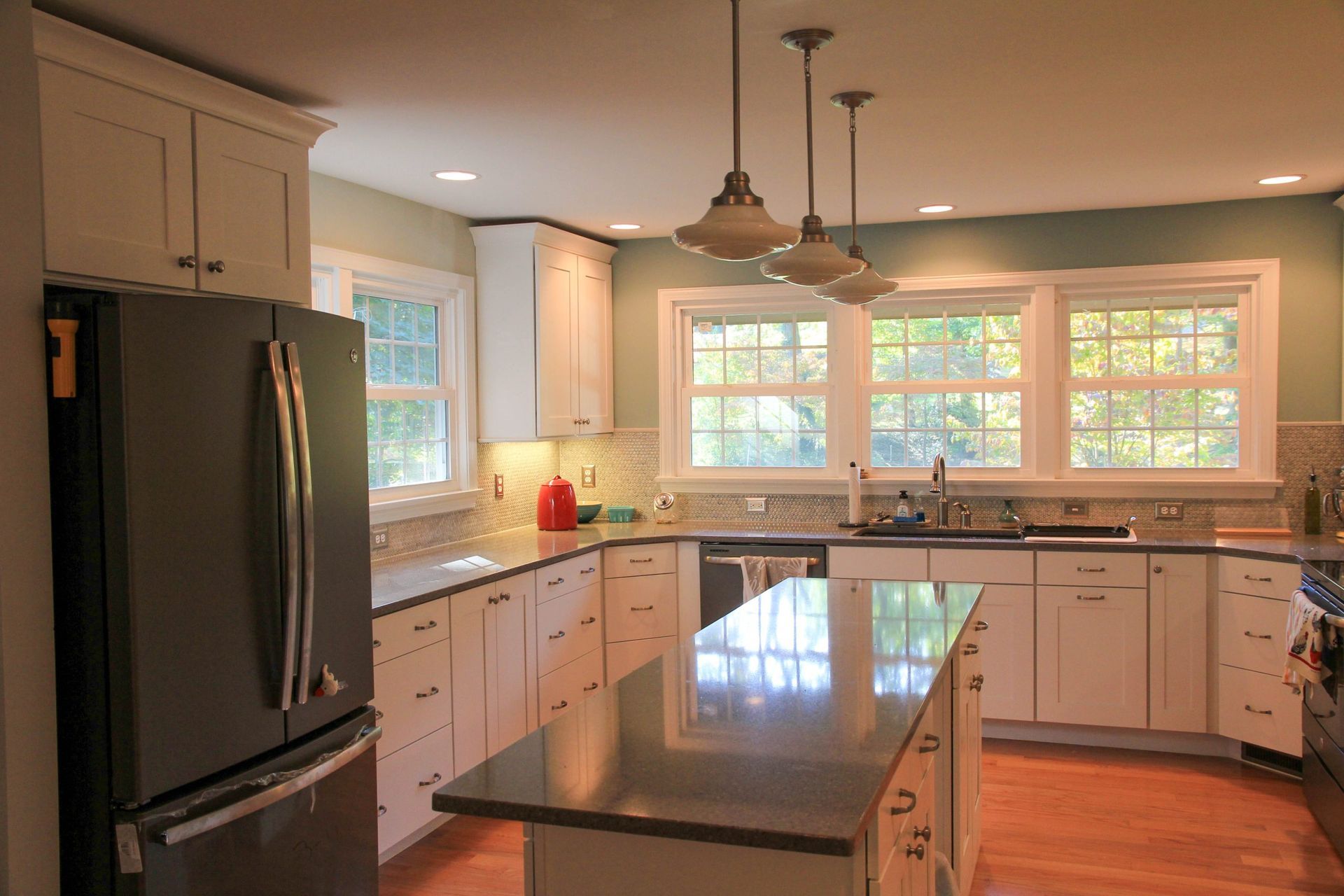 Modern kitchen with white cabinets, dark gray countertops, stainless steel refrigerator, and three pendant lights.