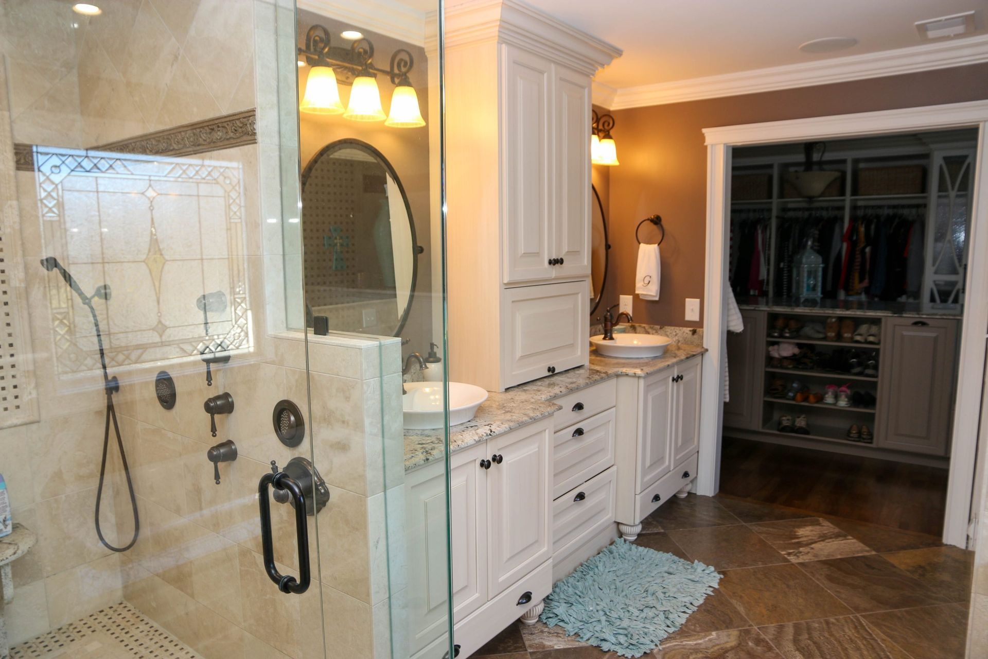 A bathroom with a stone-tiled shower, white vanity cabinets, and an adjacent walk-in closet with shelves and hanging racks.
