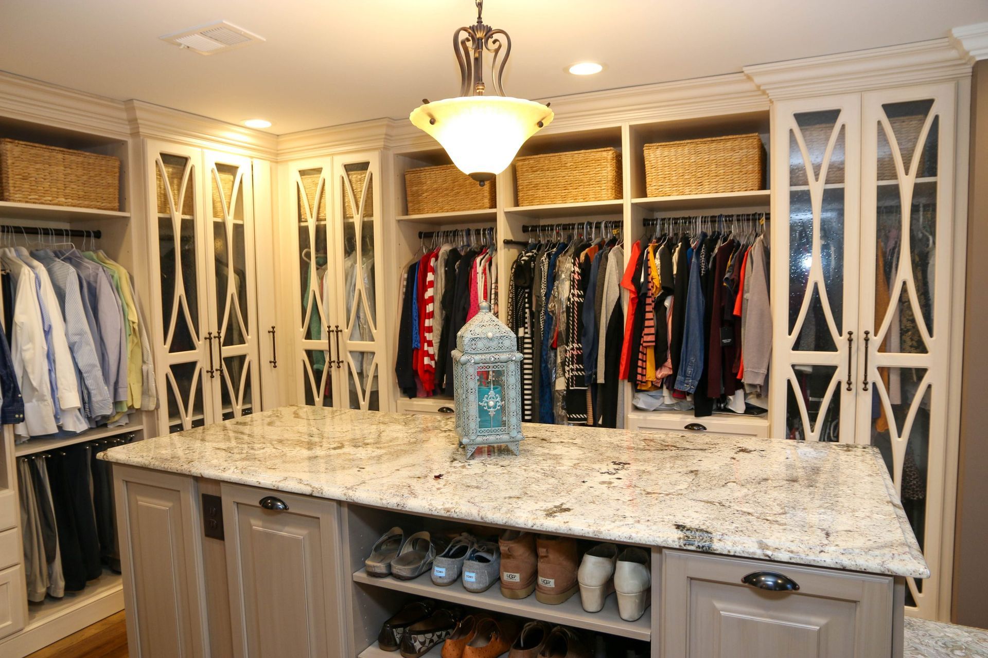 A walk-in closet featuring cream-colored cabinetry, hanging clothes, woven storage baskets, and a stone-topped center island.