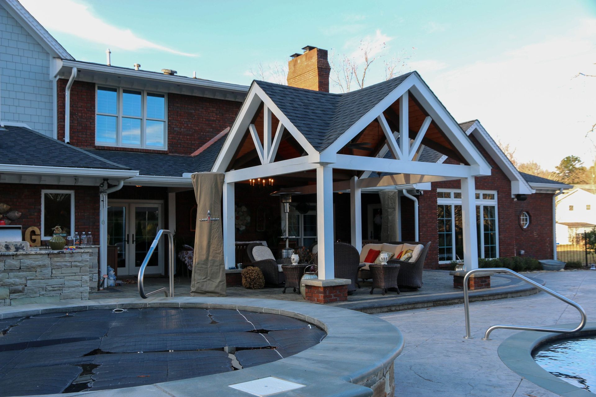 A backyard patio with a covered timber-framed structure, outdoor furniture, and a stone-trimmed swimming pool.