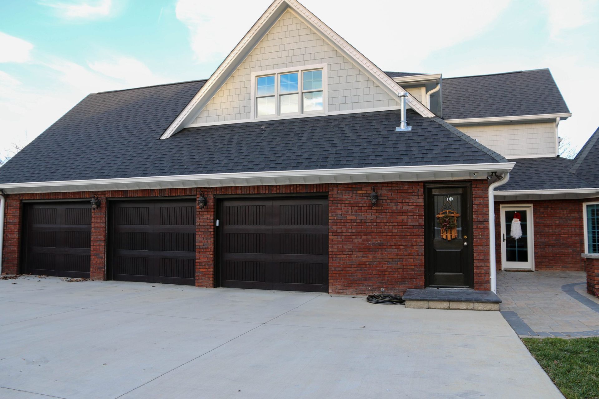 A brick, three-car garage home with a gray roof and light-colored upper siding, featuring a paved driveway.