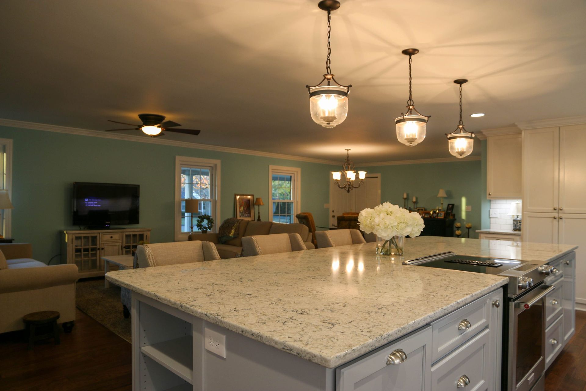 A spacious open-concept kitchen with a granite island, three pendant lights, and a view into a light blue living room.