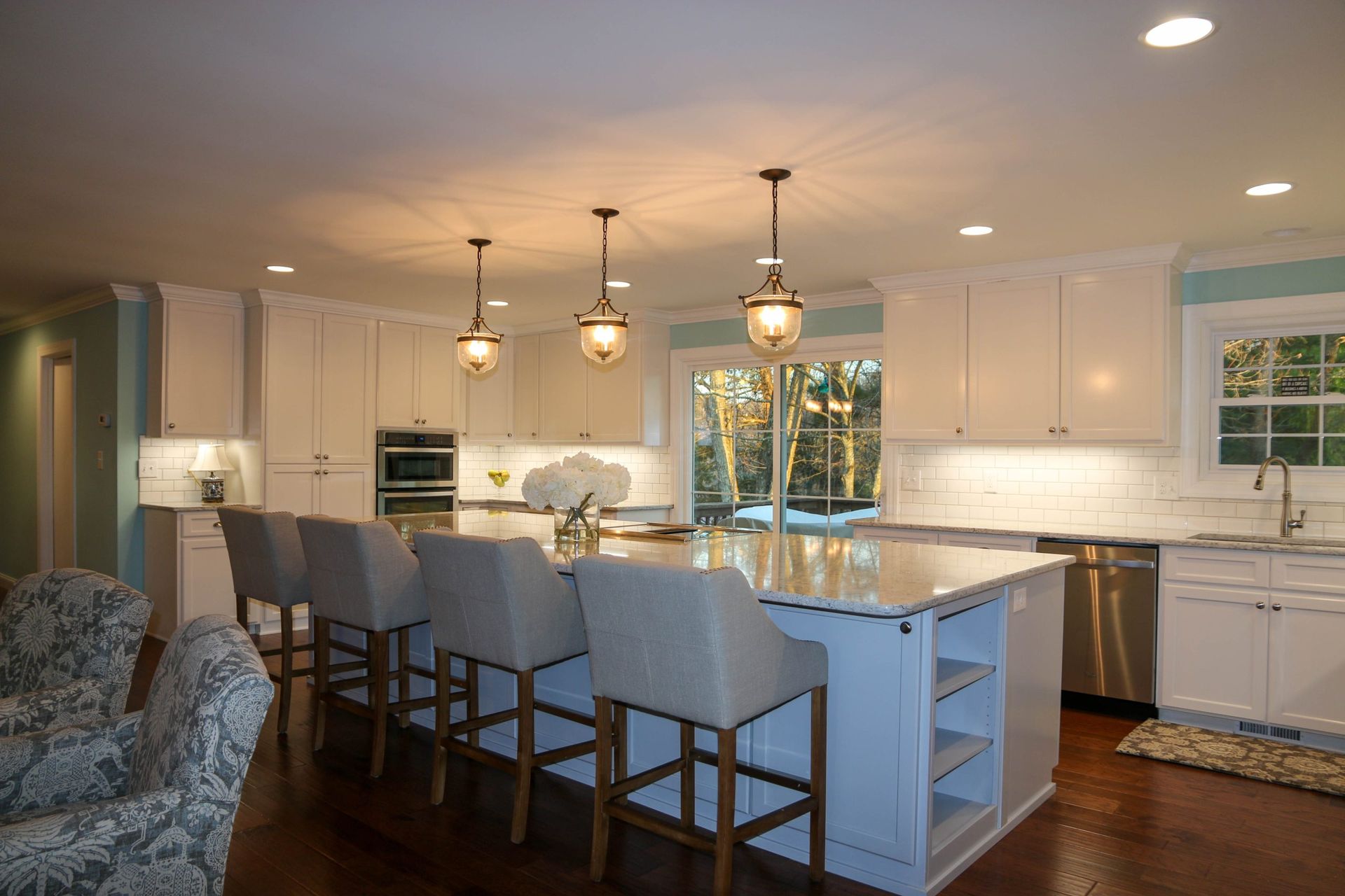 Modern kitchen with a large island featuring grey upholstered bar stools, white cabinetry, and three pendant lights.