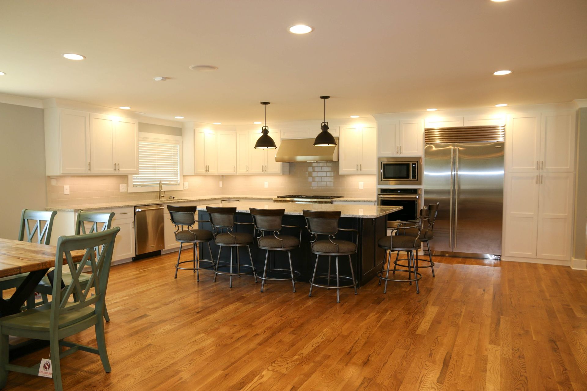 A modern kitchen with white cabinets, a black kitchen island with stools, stainless steel appliances, and wood flooring.