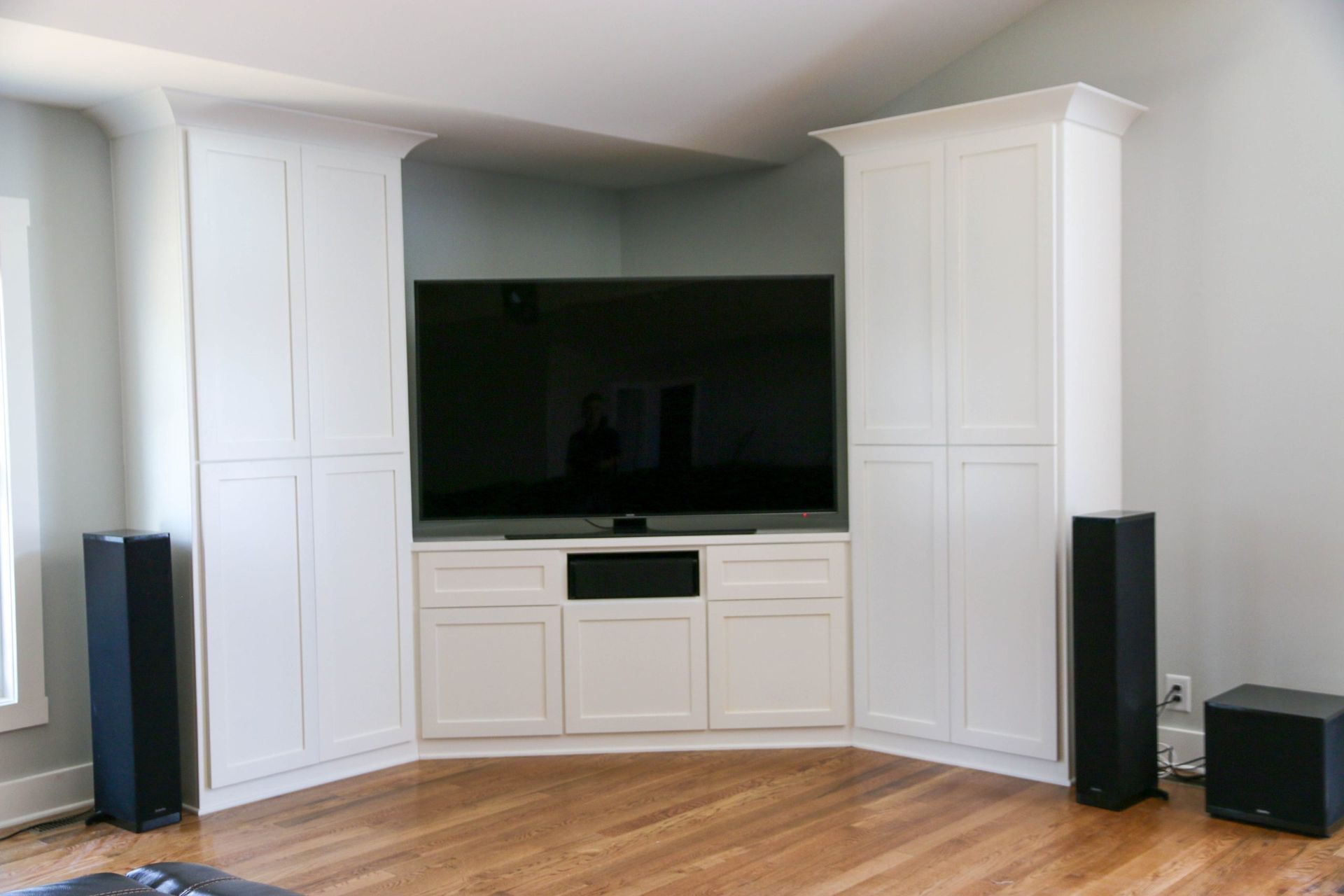 A large flat-screen TV sits on a white cabinet between two floor-to-ceiling white storage towers in a room with wood floors.