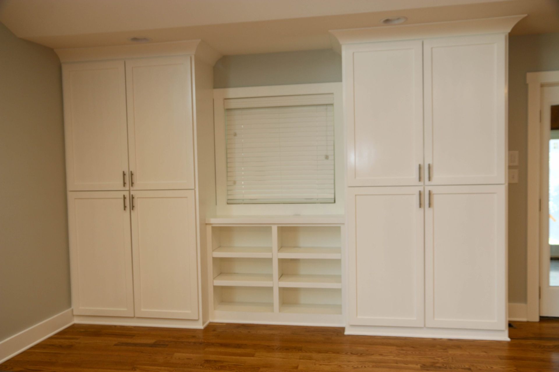 A room featuring two tall white storage cabinets flanking a central window with open shelving underneath.