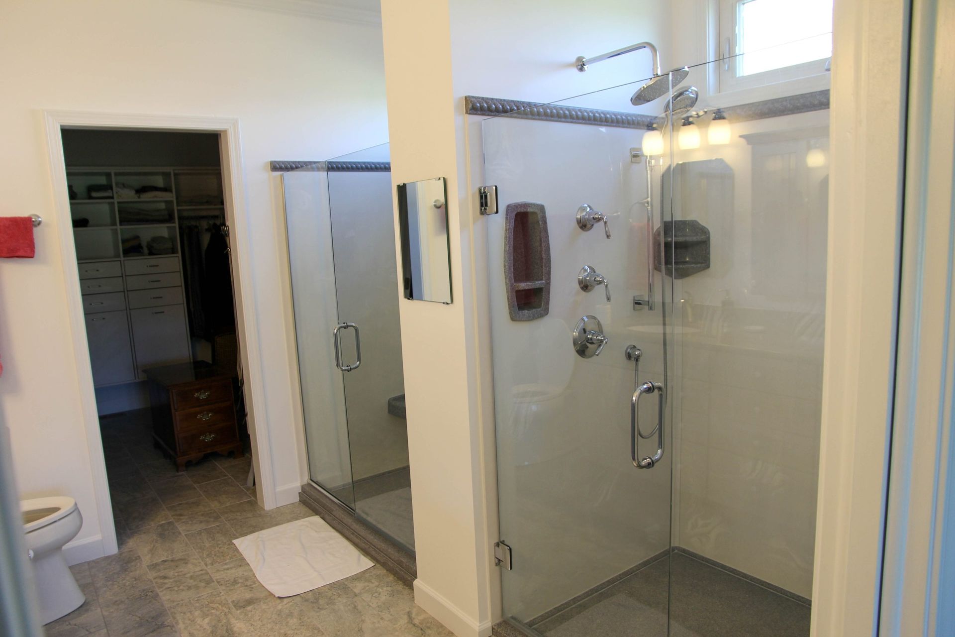 A bathroom with a large glass-enclosed shower, tile floors, and a doorway leading into a walk-in closet.