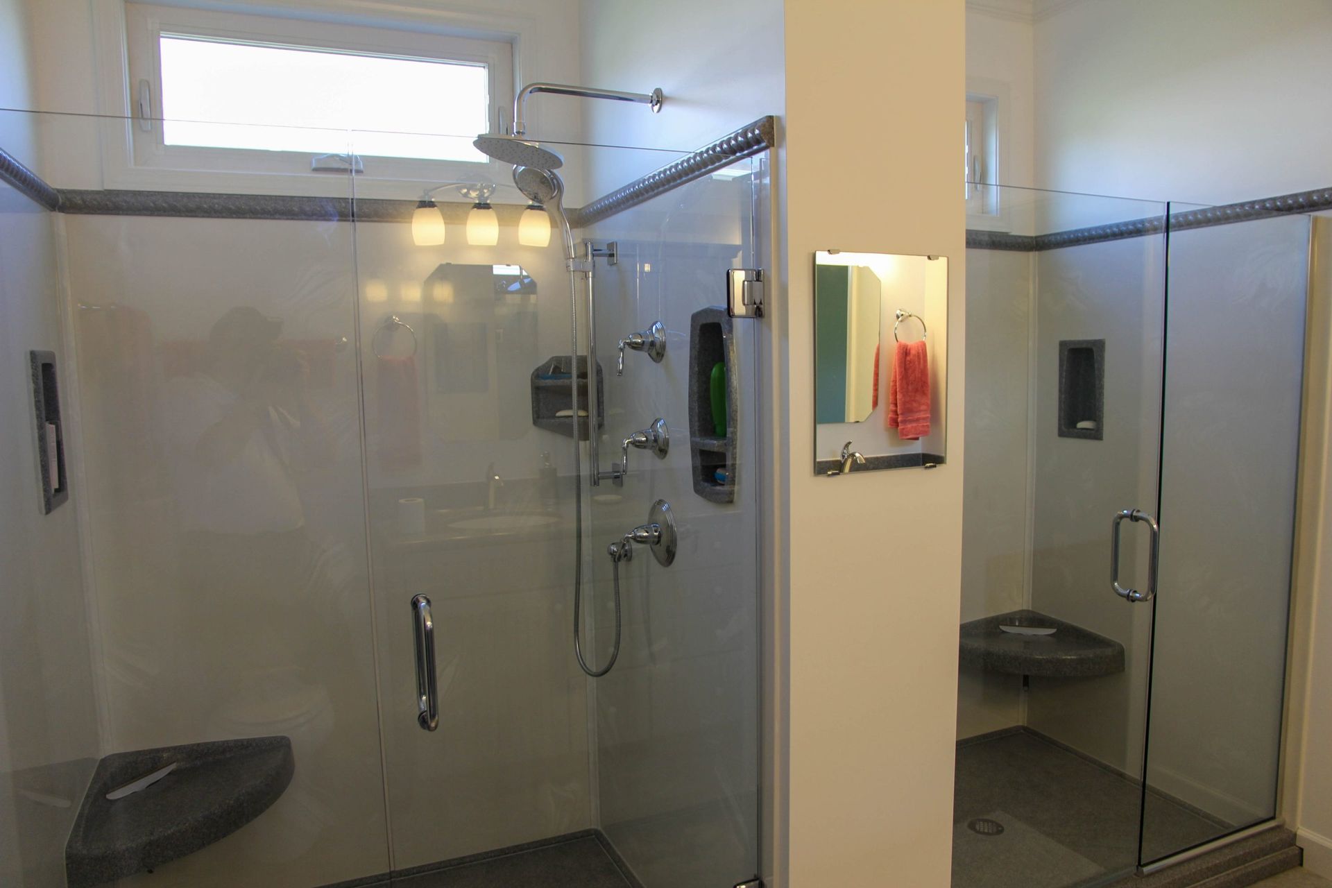 Two side-by-side walk-in showers with glass doors, neutral tile walls, corner benches, and chrome fixtures.
