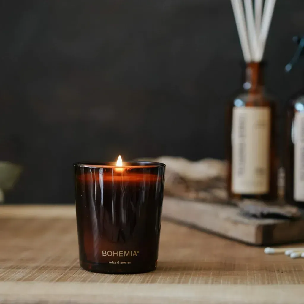 Vela encendida en vidrio marrón, junto a una caja marrón etiquetada 